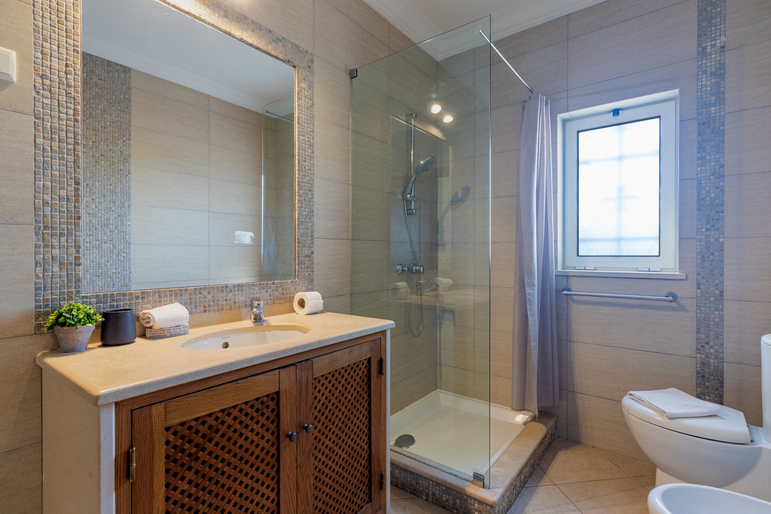 A modern bathroom with a glass-enclosed shower, a sink with a wooden cabinet, and a toilet.