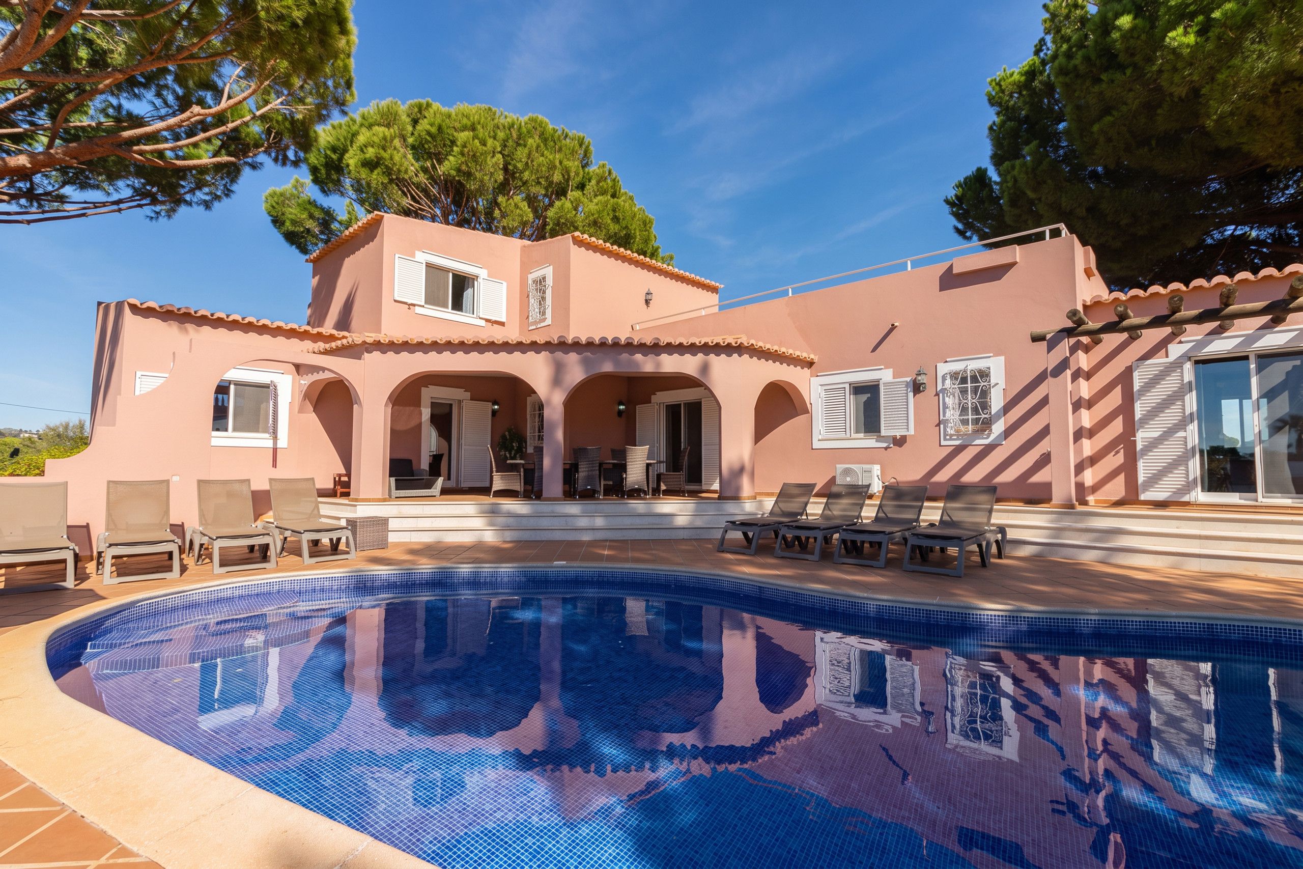 A two-story building with a swimming pool, outdoor seating, and a clear sky.