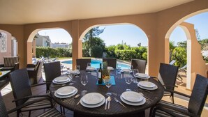 Un espace de restauration en plein air avec vue sur la piscine, aménagé avec des chaises et des tables en osier, et agrémenté d’un centre de table composé de fruits tropicaux.