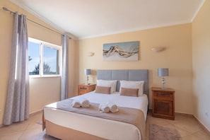 A hotel room with a bed, two bedside tables, a window with curtains, and a painting on the wall.