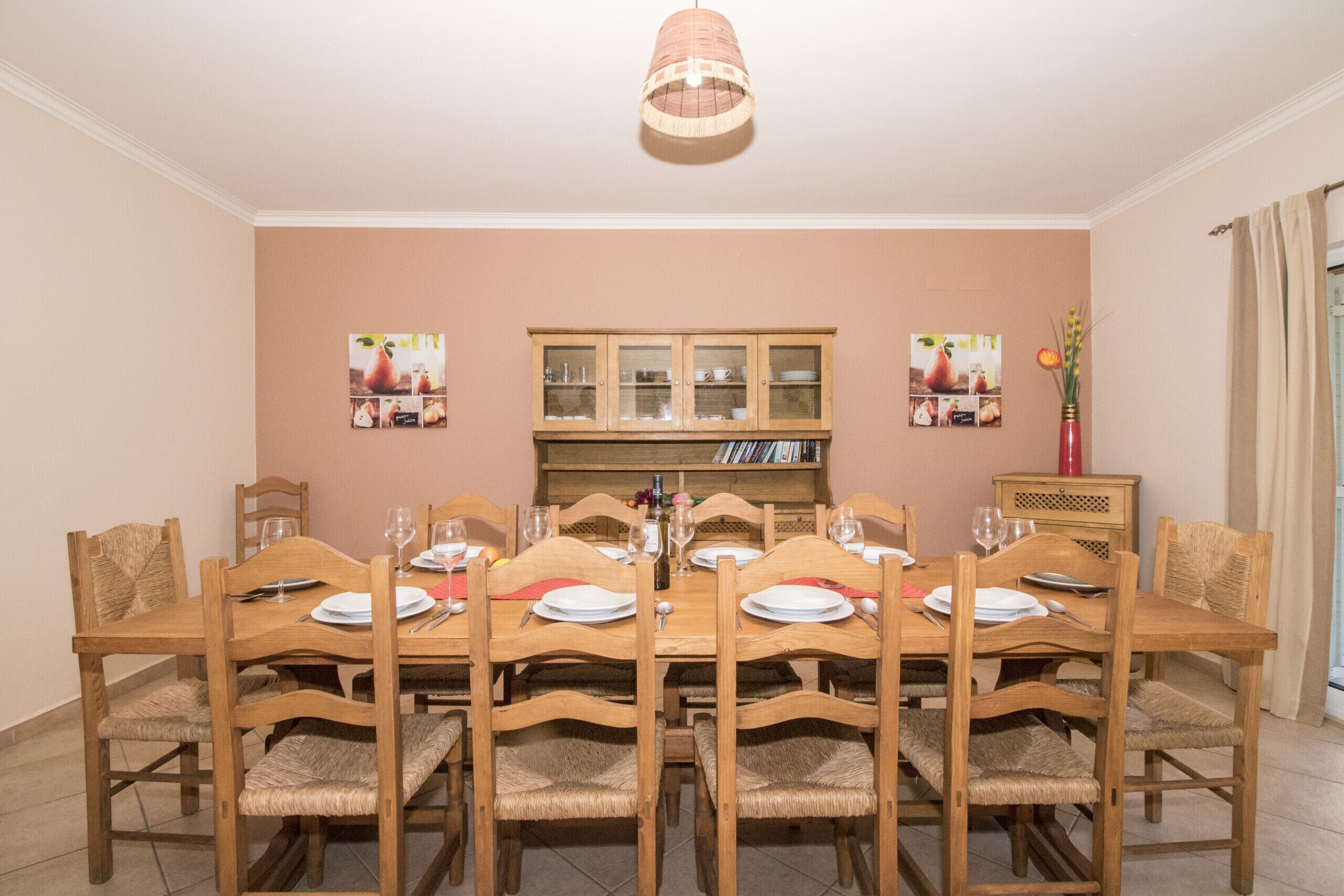 A dining room with a wooden table set for six, surrounded by wicker chairs.