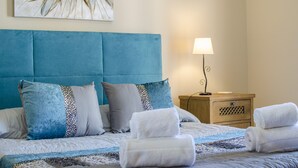 Un lit bien fait, avec une literie bleue et blanche, une lampe de chevet et une table de nuit en bois dotée d’un tiroir.
