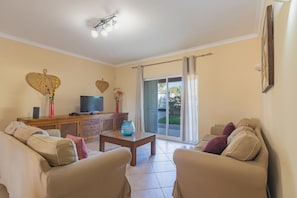 A living room with a sofa, a coffee table, a TV, and a sliding glass door leading to an outdoor area.