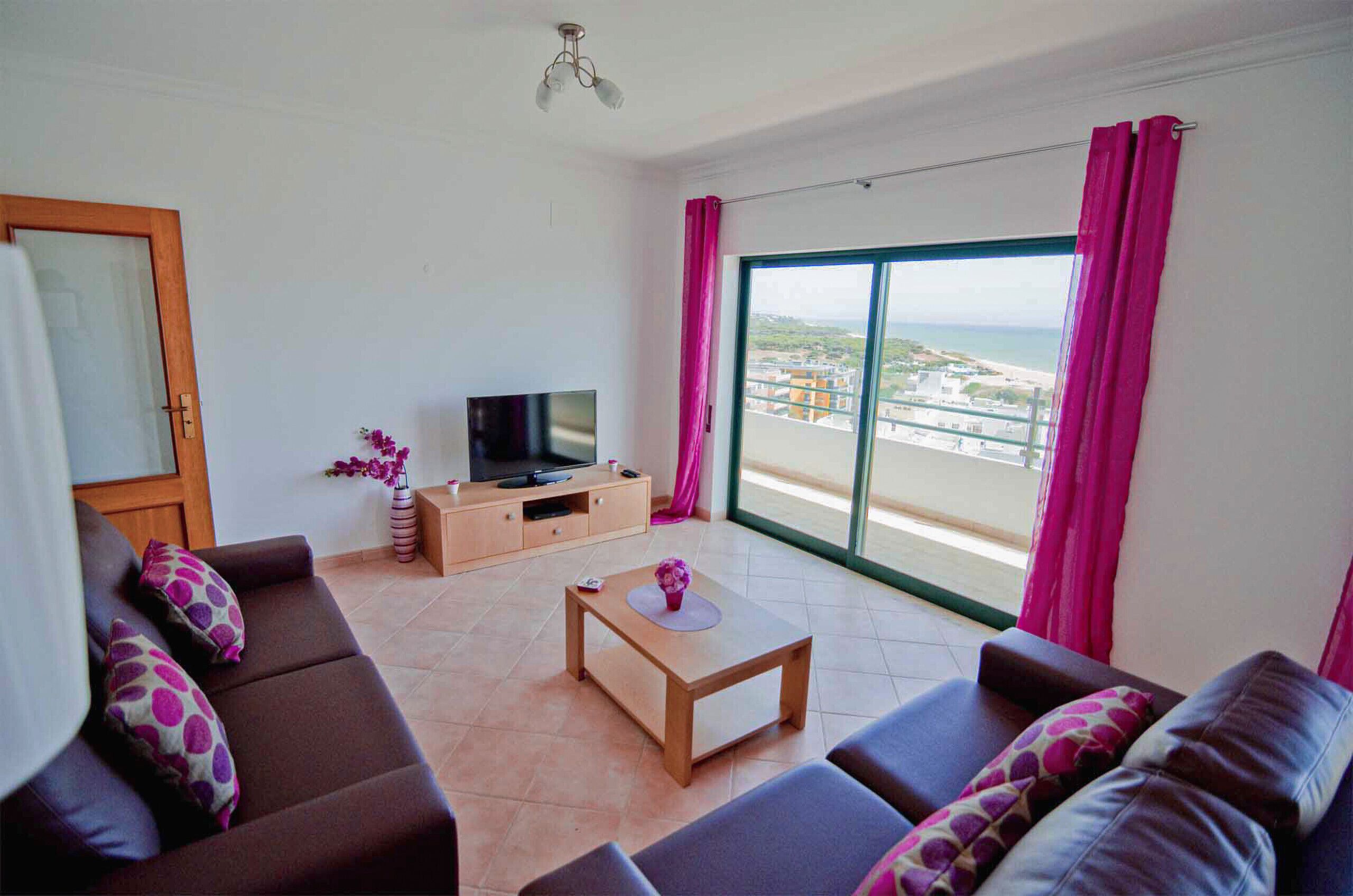 A living room with a TV, sofa, coffee table, and a view of the sea.