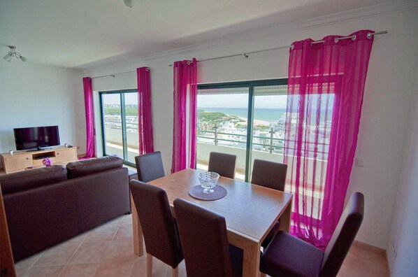 Un balcon avec vue sur la mer, une table à manger avec des chaises, un canapé et un téléviseur.