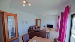 Een moderne woonkamer met een bank, een televisie en een eethoek met een tafel en stoelen.