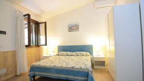 Un dormitorio con cama, mesitas de noche, aire acondicionado de pared y un pequeño cuadro.