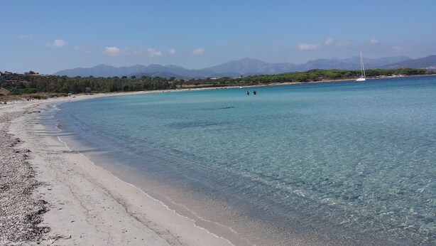 Una playa con aguas turquesas cristalinas, una orilla arenosa y montañas a lo lejos.