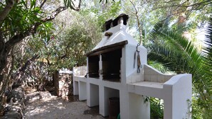 Una estructura blanca al aire libre con chimenea, rodeada de árboles y follaje.