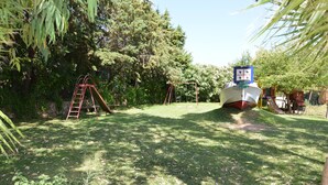 Un área con césped, un columpio, una estructura de juegos con forma de barco y una escalera.