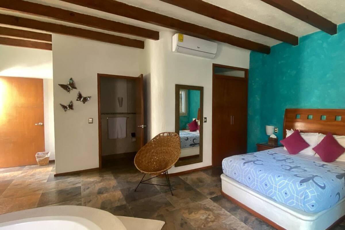 A bedroom with a bed, a chair, a bathroom, and a mirror.