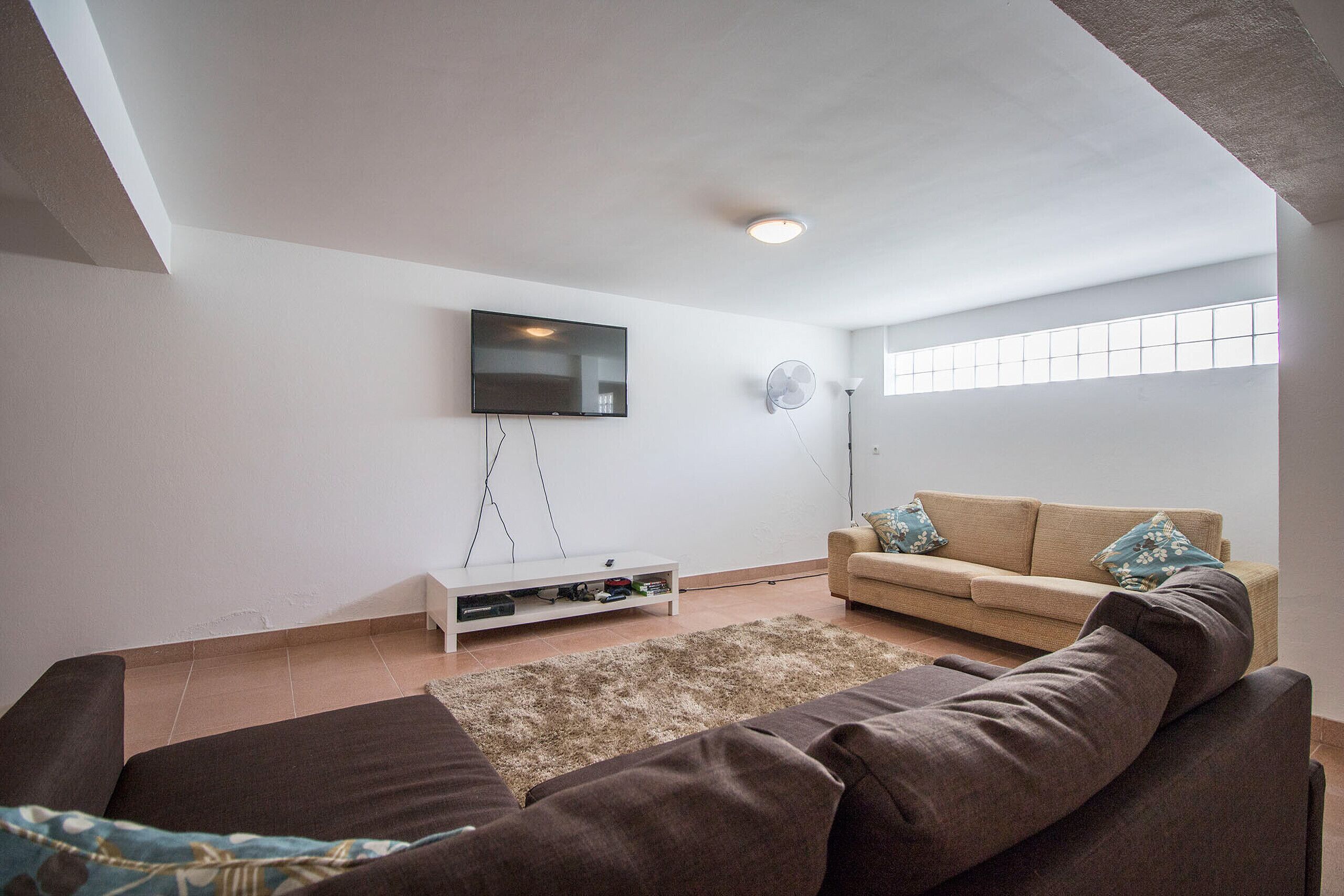 A living room with a brown sofa, a beige sofa, a flat-screen TV, a white entertainment unit, and a large window.