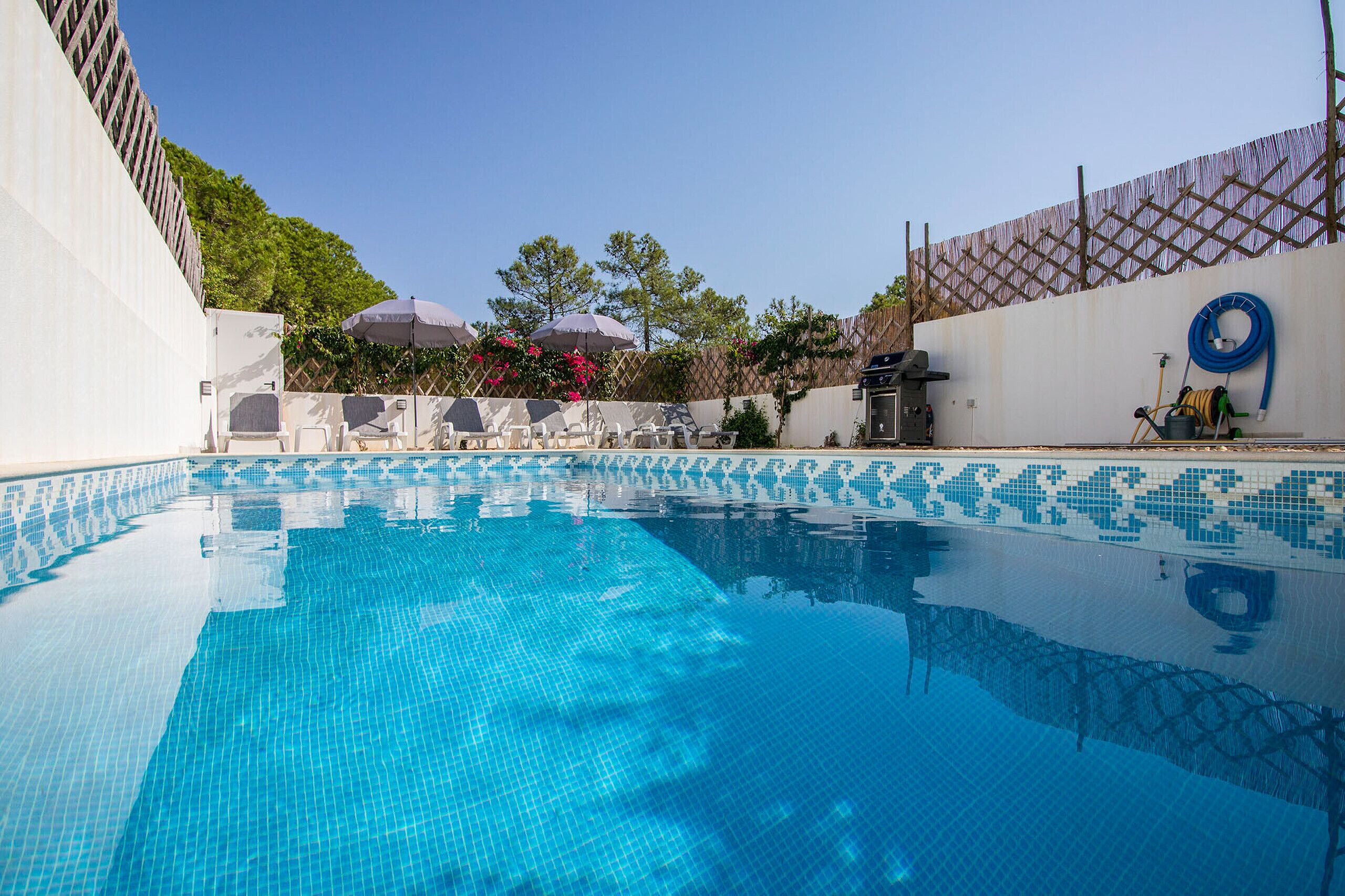 A clear blue pool with tiled edges, surrounded by a white wall with a lattice pattern, and a wooden fence.