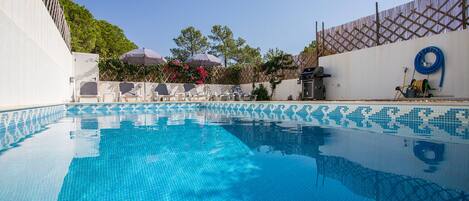 A clear blue pool with tiled edges, surrounded by a white wall with a lattice pattern, and a wooden fence.