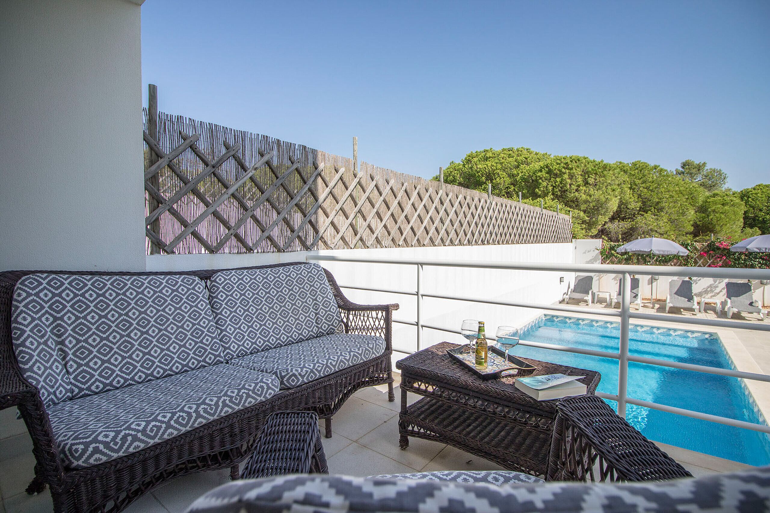 A balcony with wicker furniture, a pool, and a view of trees.