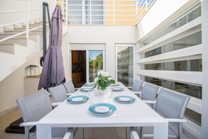 A dining area with a white table set for six, grey chairs, and a purple umbrella.