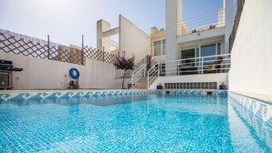 Une piscine bordée de carreaux, une clôture en bois et un bâtiment doté de balcons.