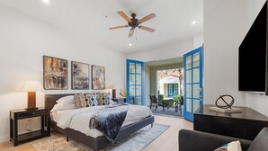 A bedroom with a bed, bedside tables, a ceiling fan, artwork, and a view through an open door.