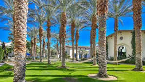 A courtyard with palm trees, a hammock, and a building with a tiled roof.