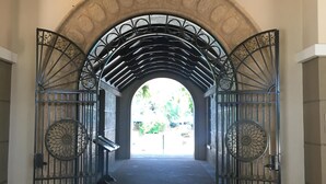 Ein Bogenbogenportal mit einer Chandelüster, Metallgitter mit Verzierungen und Blick auf Grünfläche.