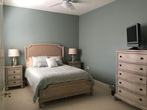 Une chambre à coucher comprenant un lit, des tables de chevet, une commode, un ventilateur de plafond et un téléviseur.