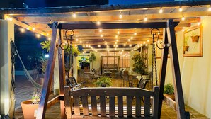 An outdoor patio area with a wooden swing set, string lights, and potted plants. - Hotel Barcelona (Ponta Pora)