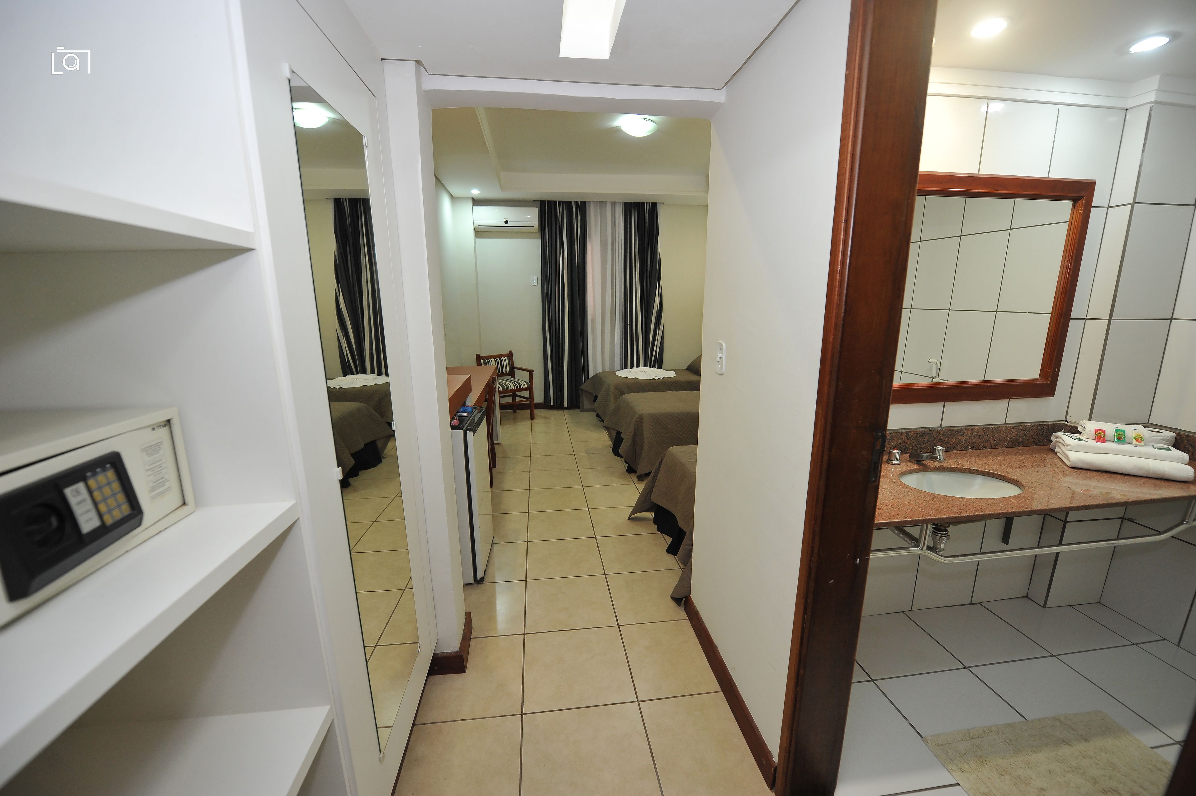 Habitación de hotel con cama, escritorio, silla, mesita, espejo, lavabo y zona de ducha.