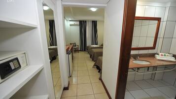 Habitación de hotel con cama, escritorio, silla, mesita, espejo, lavabo y zona de ducha.