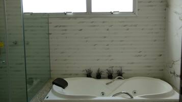 Un baño con cabina de ducha de vidrio, una bañera independiente y una ventana sobre la bañera.