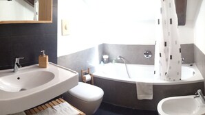 A modern bathroom with a double sink, a bathtub, and a bidet.