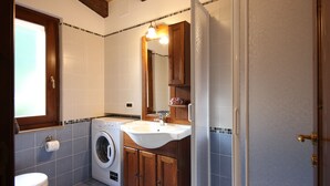 Et lille badeværelse med vaskemaskine, håndvask og toilet.