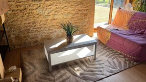 A room with a stone wall, a white table with a plant, a patterned rug, and a purple sofa.