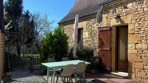 A stone building with a gravel patio and a green table with chairs.