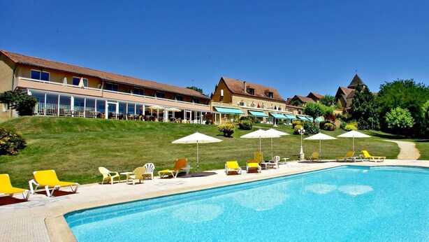 A swimming pool with lounge chairs and umbrellas, a building with a terrace, and a clear sky.