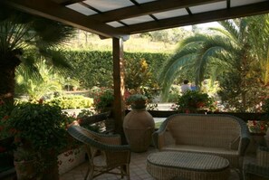 A covered patio with wicker furniture, a large vase, and lush greenery.