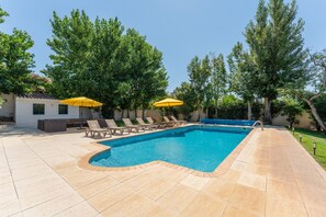 Une piscine entourée d’arbres, avec des chaises longues et des parasols jaunes.