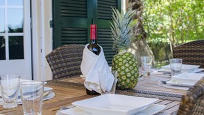 A dining table set with plates, glasses, and a bottle of wine, with a pineapple and a wrapped bottle on the table.