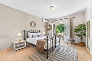A bedroom with a bed, bedside tables, a lamp, a mirror, an air conditioning unit, a door leading to a balcony, and a potted plant. - Villa Caravela | 4 Bedrooms | Beautiful Garden | Almancil (Almancil)