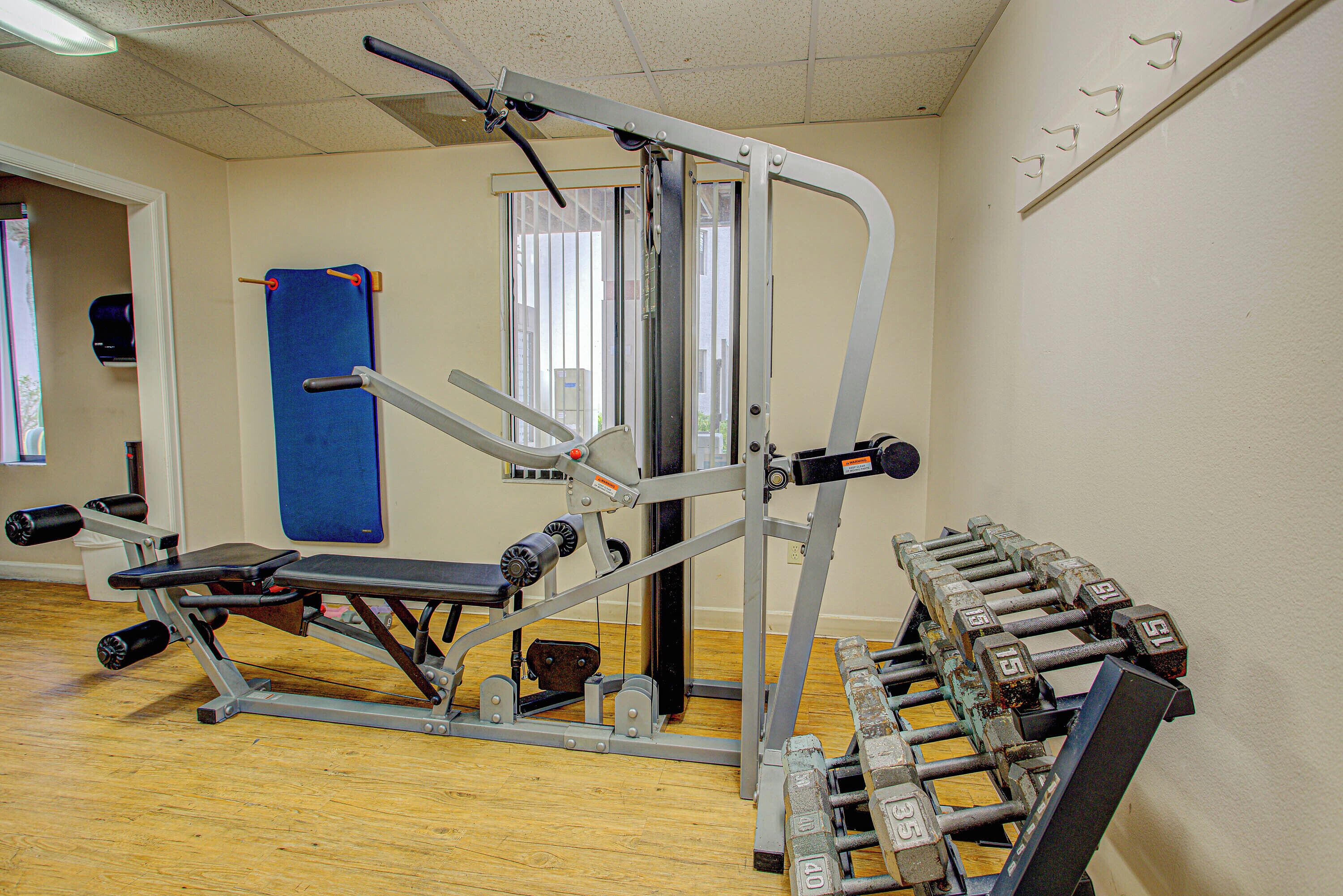 A gym with a bench press, dumbbells, and a blue mat.
