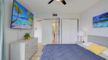 Un dormitorio con cama, ventilador de techo, televisor y obras de arte en las paredes.