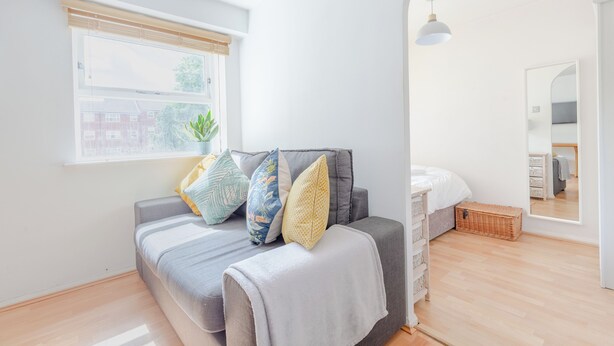 Une chambre à coucher moderne avec un lit, une fenêtre avec des stores, une table de chevet, un miroir et un plancher en bois.
