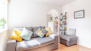 Un salon moderne avec un canapé gris, un petit pouf gris et une bibliothèque.