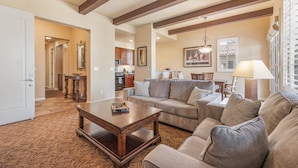 A living room with a sofa, a coffee table, and a lamp. There is a kitchen in the background.