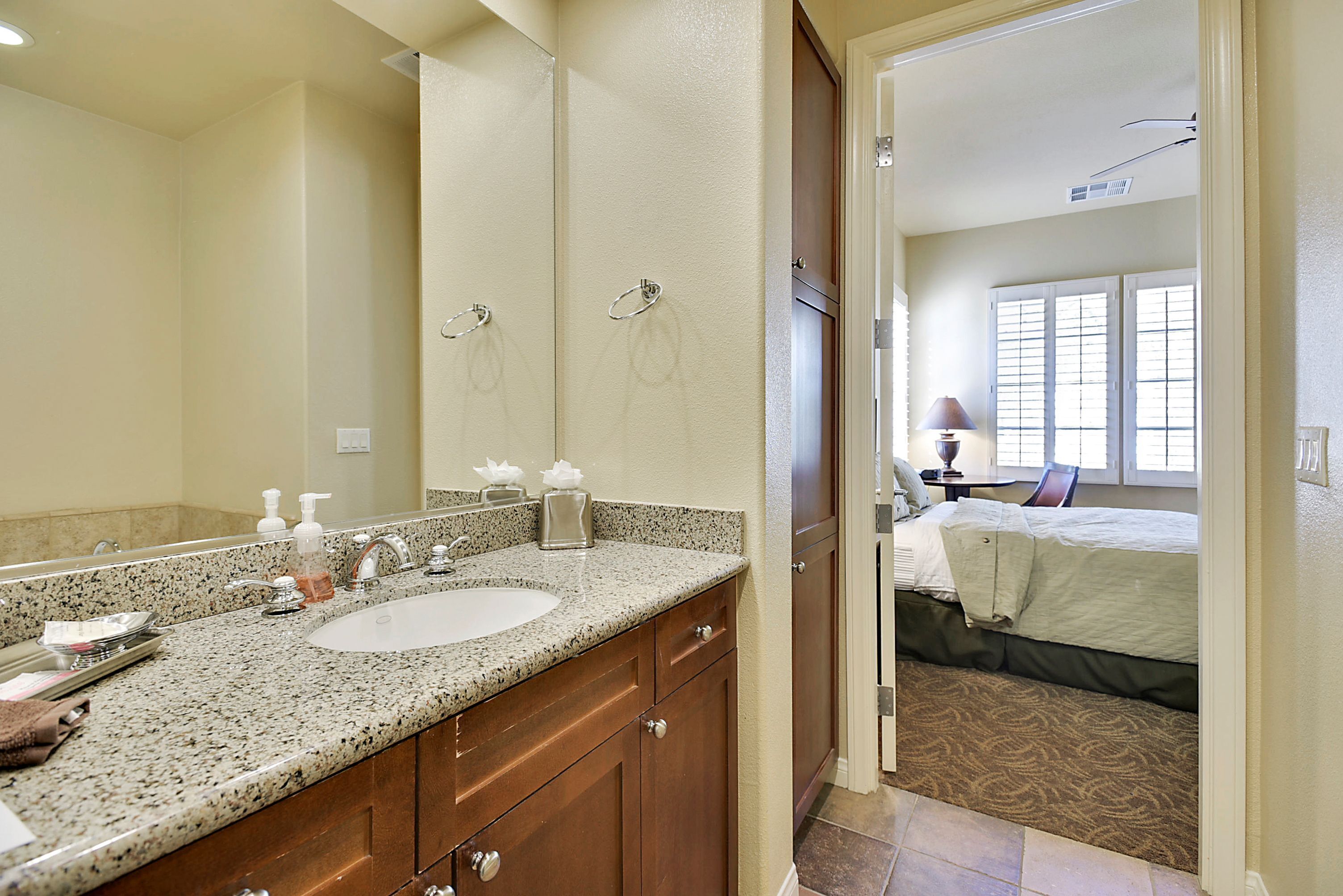 A bathroom with a granite countertop sink, a large mirror, and wooden cabinets.