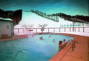 Una piscina con persone al suo interno, circondata da un paesaggio innevato e una recinzione.