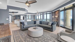 A spacious living room with a large sectional sofa, a round coffee table, and a ceiling fan. - The Oasis At Orange Beach 2911 by Liquid Life (Orange Beach)