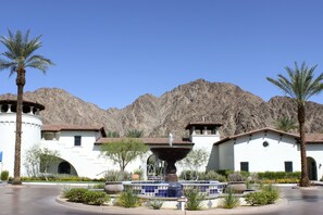 A building with a fountain, palm trees, and mountains in the background.