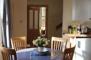A dining area with a table set for four, a vase of flowers, and a kitchen area with a refrigerator and cabinets.