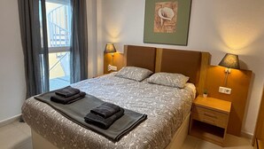 A neatly made bed with a patterned bedspread and two folded towels, a bedside table with a lamp, a framed picture on the wall, and a window with curtains. - The Best Condo in Vera with a fantastic View (Vera)