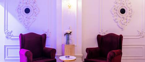 A room with two red velvet armchairs, a small round table, and a vase with flowers.